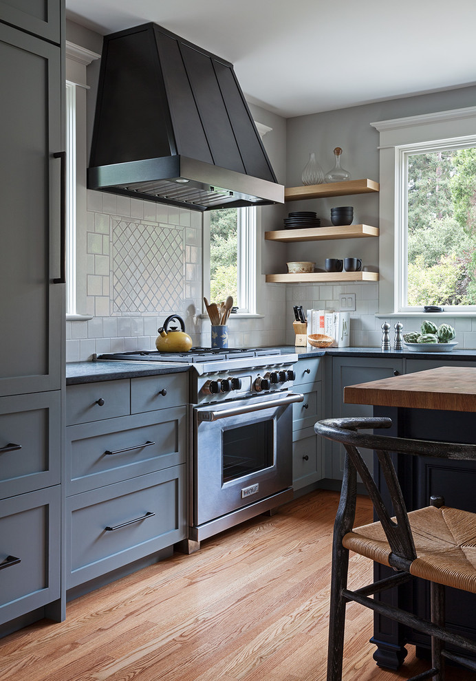 Inspiration for a medium sized classic l-shaped enclosed kitchen in San Francisco with a belfast sink, shaker cabinets, grey cabinets, soapstone worktops, white splashback, ceramic splashback, stainless steel appliances, light hardwood flooring, an island and beige floors.