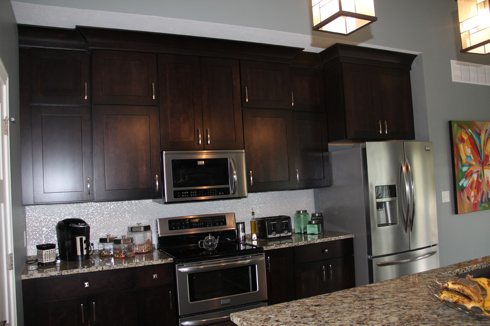 Amerikansk inredning av ett kök, med en undermonterad diskho, granitbänkskiva, vitt stänkskydd, rostfria vitvaror, klinkergolv i keramik och en köksö