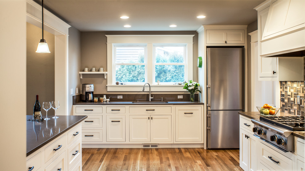 Inspiration for a mid-sized craftsman u-shaped medium tone wood floor eat-in kitchen remodel in Portland with white cabinets, gray backsplash, glass tile backsplash, stainless steel appliances, a peninsula, an undermount sink, shaker cabinets and soapstone countertops