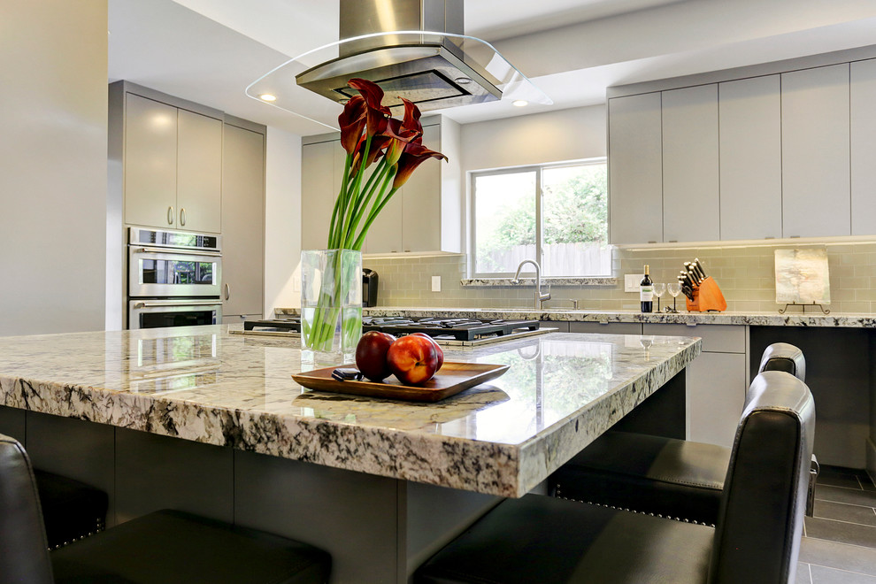 Modern inredning av ett stort kök, med en undermonterad diskho, släta luckor, grå skåp, granitbänkskiva, grått stänkskydd, stänkskydd i glaskakel, rostfria vitvaror, klinkergolv i keramik och en köksö