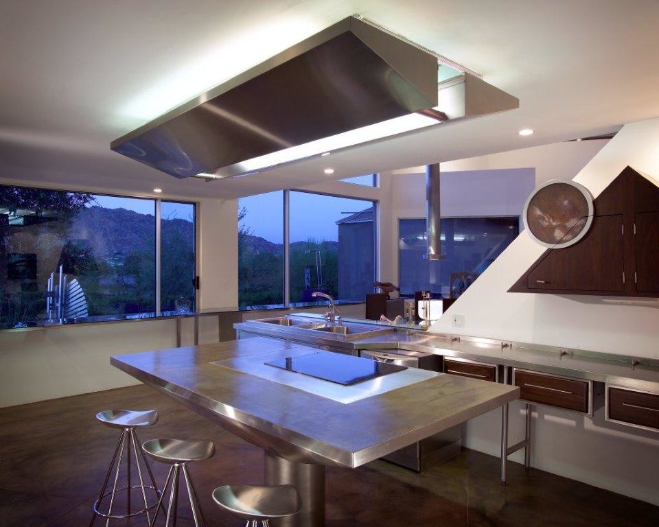 Modern inredning av ett kök, med en trippel diskho, skåp i mörkt trä, bänkskiva i rostfritt stål, vitt stänkskydd, rostfria vitvaror och en köksö