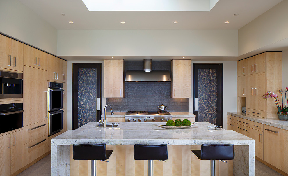 Modern inredning av ett kök, med en undermonterad diskho, släta luckor, skåp i ljust trä, grått stänkskydd, rostfria vitvaror och en köksö