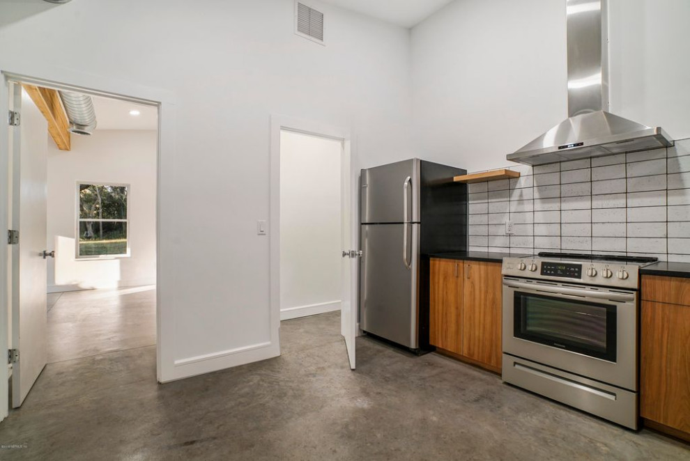 Foto på ett stort funkis svart kök, med en integrerad diskho, släta luckor, skåp i mellenmörkt trä, bänkskiva i kvartsit, vitt stänkskydd, stänkskydd i cementkakel, rostfria vitvaror, betonggolv och grått golv