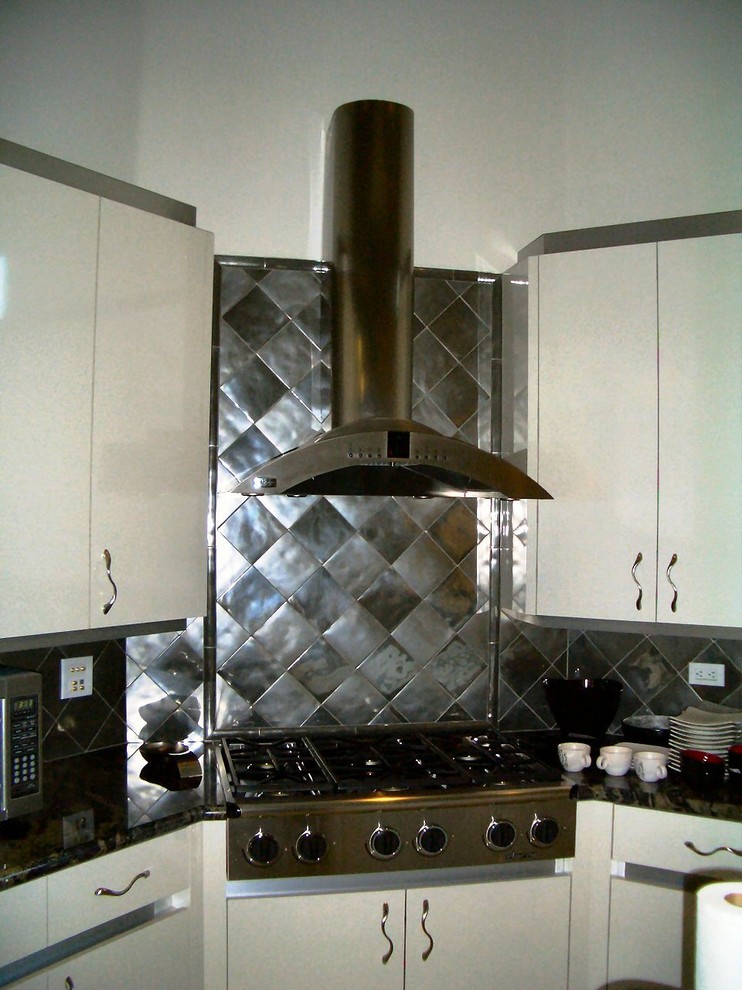 Idéer för ett stort modernt kök, med en undermonterad diskho, släta luckor, skåp i rostfritt stål, granitbänkskiva, stänkskydd med metallisk yta, stänkskydd i porslinskakel, rostfria vitvaror, kalkstensgolv och en köksö