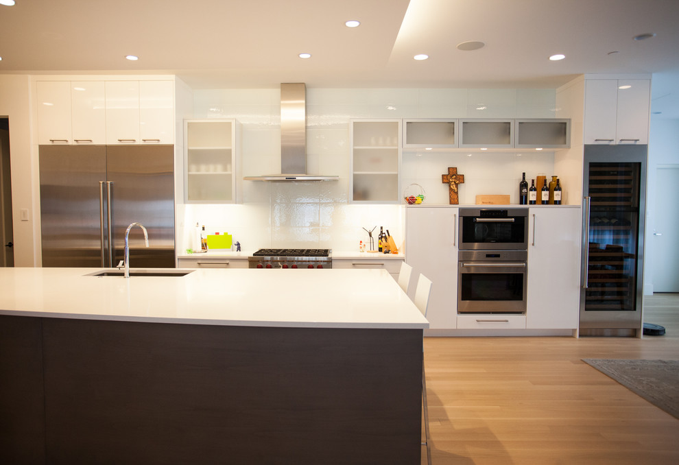 Foto de cocina comedor lineal moderna de tamaño medio con armarios con paneles lisos, puertas de armario blancas, salpicadero de azulejos de vidrio, electrodomésticos de acero inoxidable y una isla