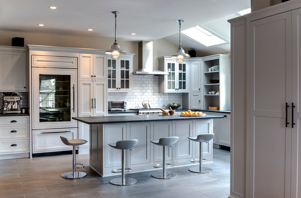 Example of a large minimalist l-shaped light wood floor and gray floor eat-in kitchen design in Boston with shaker cabinets, white cabinets, white backsplash, subway tile backsplash, an island, a farmhouse sink and paneled appliances