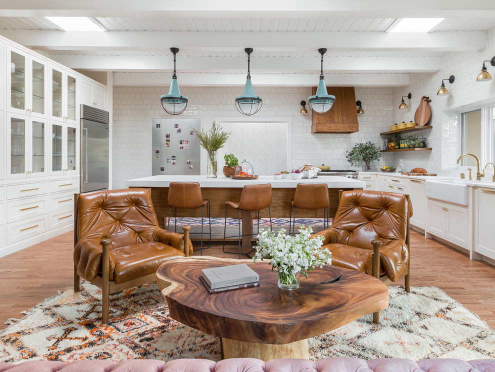 Eclectic open plan kitchen in Albuquerque with a belfast sink, white cabinets, white splashback, stainless steel appliances, medium hardwood flooring, an island, recessed-panel cabinets and ceramic splashback.