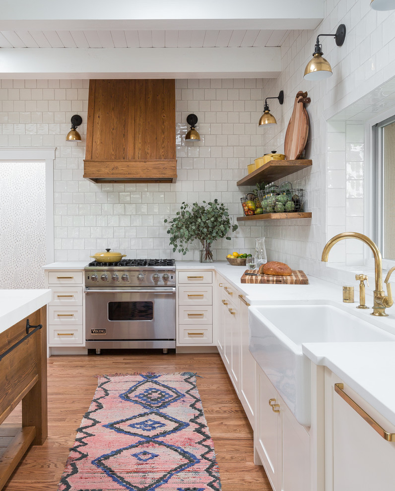 Foto på ett funkis kök, med en rustik diskho, luckor med infälld panel, vita skåp, vitt stänkskydd, stänkskydd i keramik, rostfria vitvaror, mellanmörkt trägolv, bänkskiva i kvartsit och en köksö