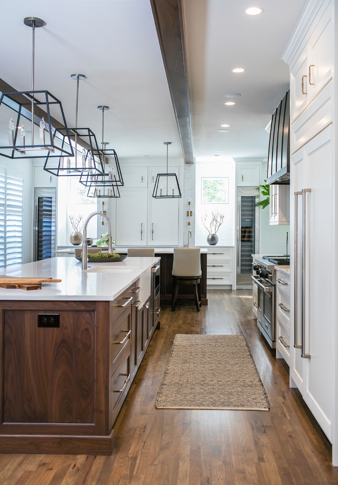 Photo of a large classic galley kitchen/diner in Denver with recessed-panel cabinets, white cabinets, engineered stone countertops, stainless steel appliances, medium hardwood flooring, brown floors, a submerged sink and an island.