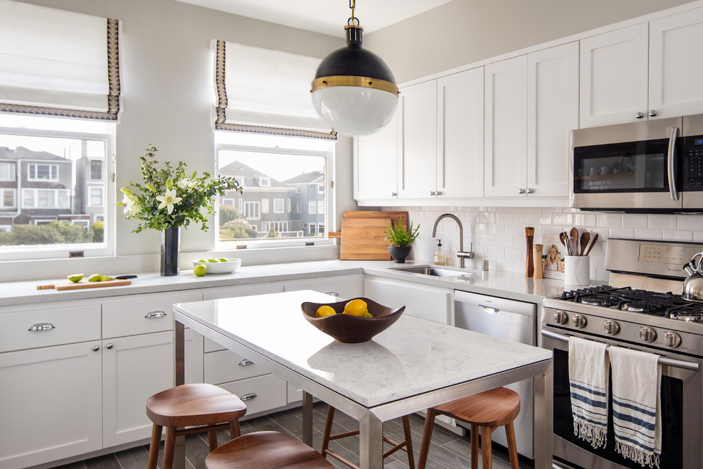 Transitional l-shaped brown floor kitchen photo in Sacramento with an undermount sink, shaker cabinets, white cabinets, white backsplash, subway tile backsplash, stainless steel appliances, an island and gray countertops