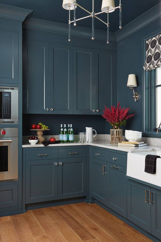 Idée de décoration pour une cuisine tradition avec un placard à porte shaker, des portes de placard bleues, une crédence bleue, un électroménager en acier inoxydable, un sol en bois brun et un sol marron.