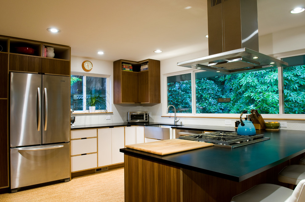 This is an example of a modern u-shaped kitchen/diner in Seattle with a belfast sink, flat-panel cabinets, dark wood cabinets, white splashback, ceramic splashback and stainless steel appliances.