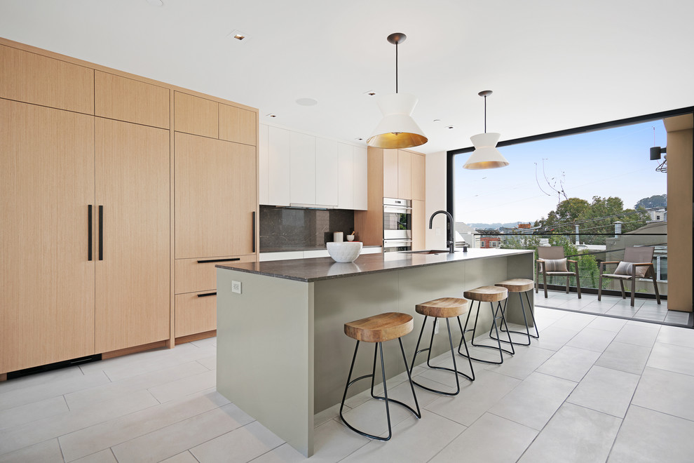 This is an example of a large contemporary galley kitchen/diner in San Francisco with a built-in sink, light wood cabinets, black splashback, stainless steel appliances, an island, grey floors, flat-panel cabinets and marble splashback.