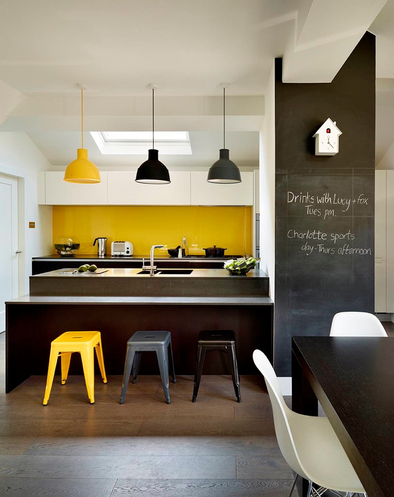 Exempel på ett mellanstort modernt grå grått kök, med släta luckor, vita skåp, gult stänkskydd, mörkt trägolv, en dubbel diskho, glaspanel som stänkskydd, en halv köksö och brunt golv