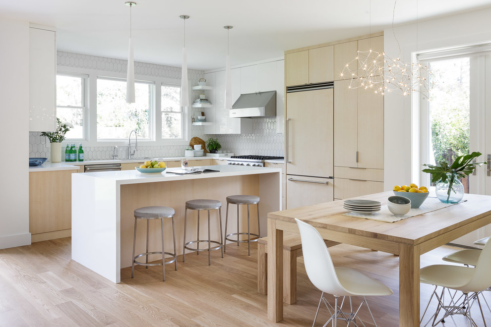 Design ideas for a medium sized contemporary l-shaped open plan kitchen in Sacramento with flat-panel cabinets, light wood cabinets, white splashback, integrated appliances, light hardwood flooring, an island, beige floors, a built-in sink and ceramic splashback.