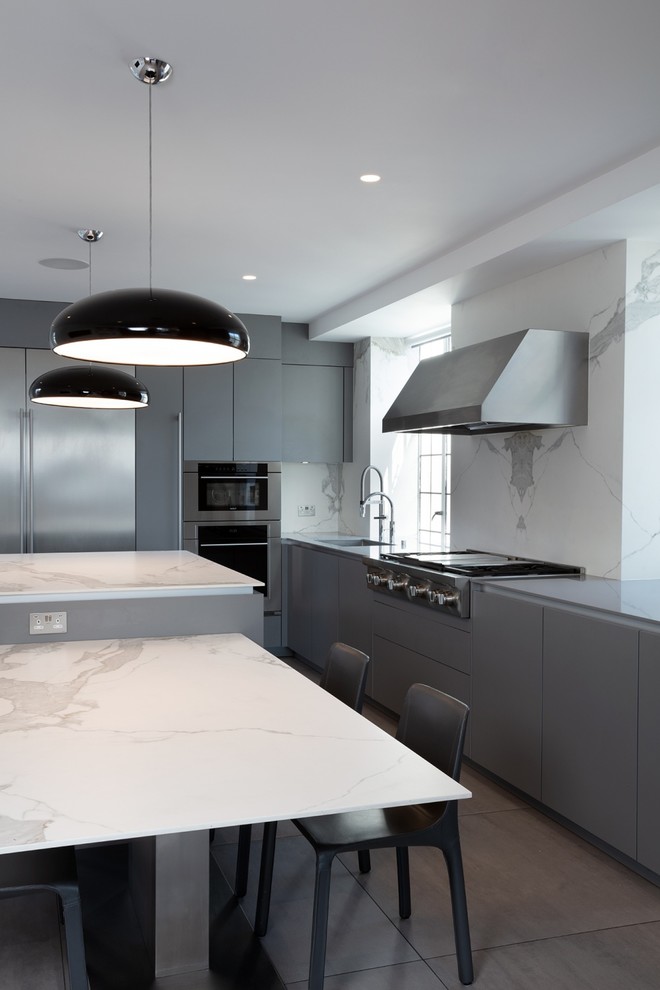 This is an example of a large contemporary l-shaped kitchen/diner in London with a built-in sink, flat-panel cabinets, grey cabinets, engineered stone countertops, white splashback, stone slab splashback, stainless steel appliances, ceramic flooring, an island, grey floors and white worktops.