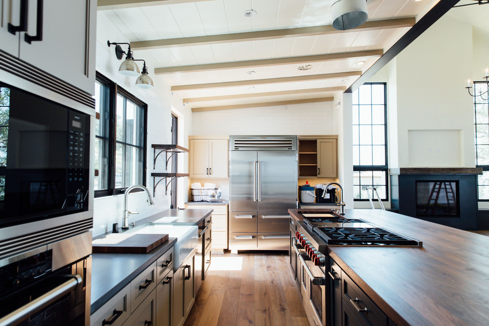 Imagen de cocina clásica renovada con armarios estilo shaker, electrodomésticos de acero inoxidable, suelo de madera clara y una isla