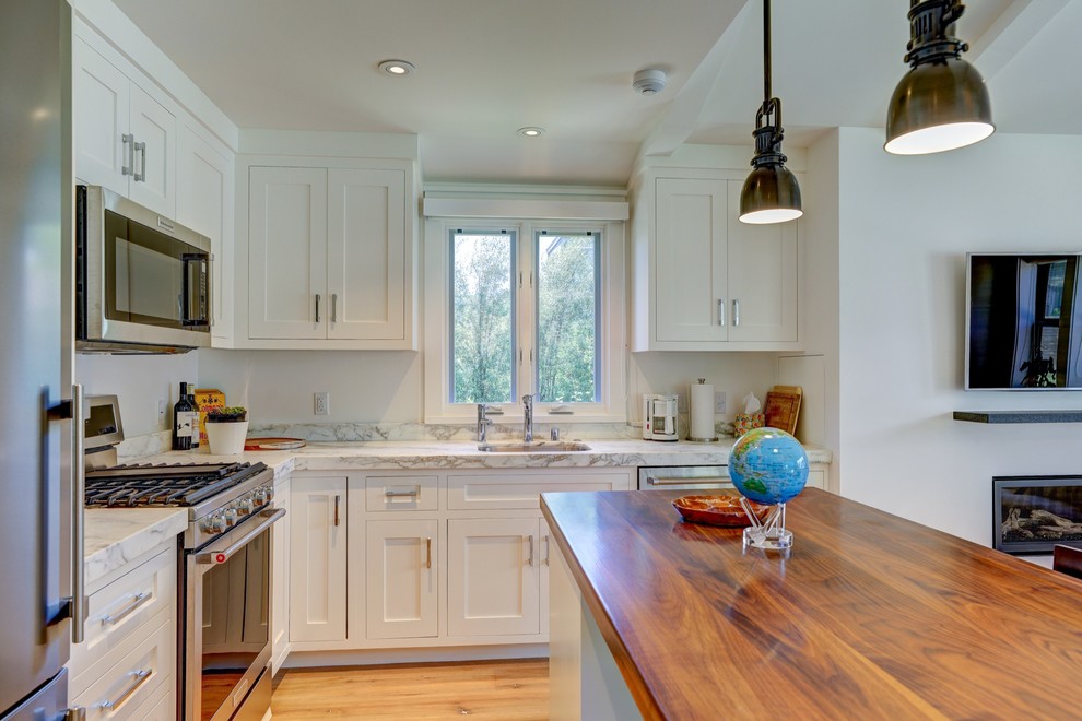 Bild på ett litet lantligt kök, med en undermonterad diskho, släta luckor, vita skåp, träbänkskiva, vitt stänkskydd, stänkskydd i marmor, rostfria vitvaror, ljust trägolv, en köksö och beiget golv