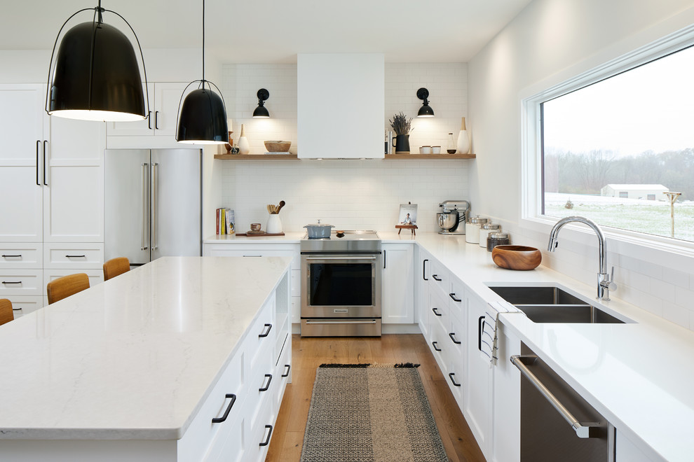 Diseño de cocina comedor campestre con puertas de armario blancas, encimera de laminado, electrodomésticos de acero inoxidable, suelo de madera clara, una isla y encimeras blancas