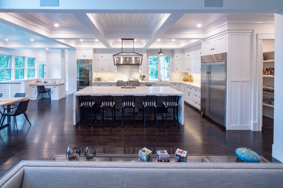 Eat-in kitchen - large cottage single-wall dark wood floor eat-in kitchen idea in Boston with a farmhouse sink, recessed-panel cabinets, white cabinets, quartz countertops, white backsplash, stone slab backsplash, stainless steel appliances, an island and white countertops