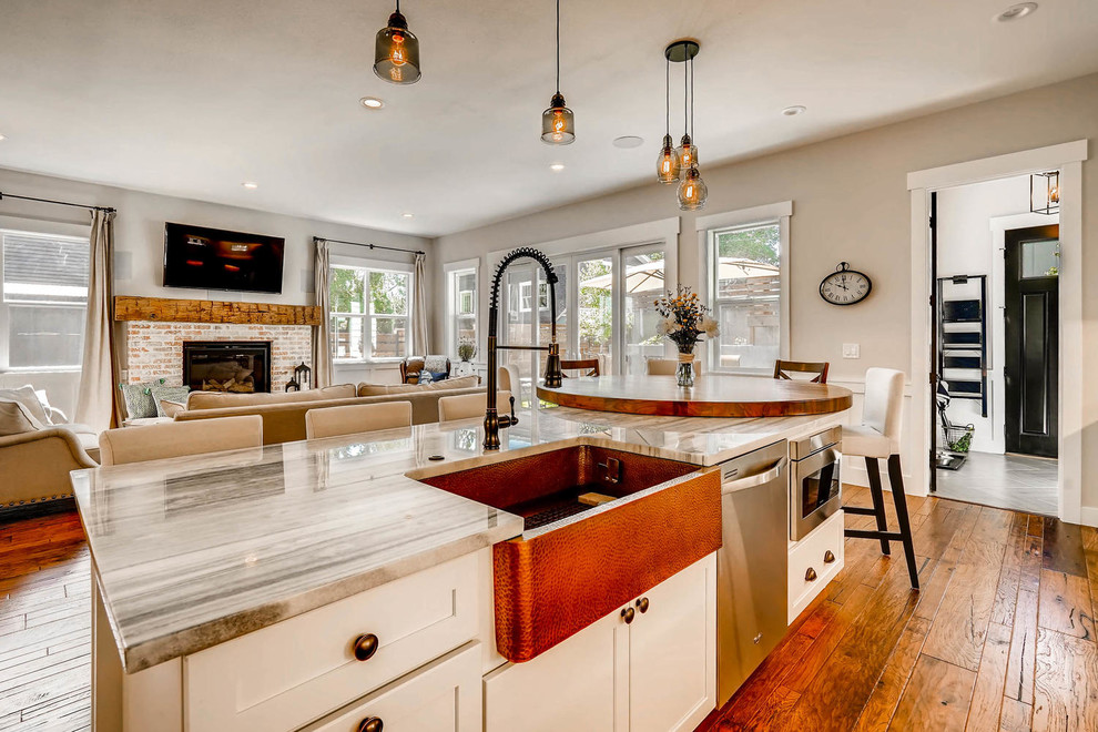 Example of a large cottage single-wall medium tone wood floor and brown floor open concept kitchen design in Denver with a farmhouse sink, shaker cabinets, white cabinets, quartz countertops, white backsplash, glass tile backsplash, stainless steel appliances, an island and white countertops