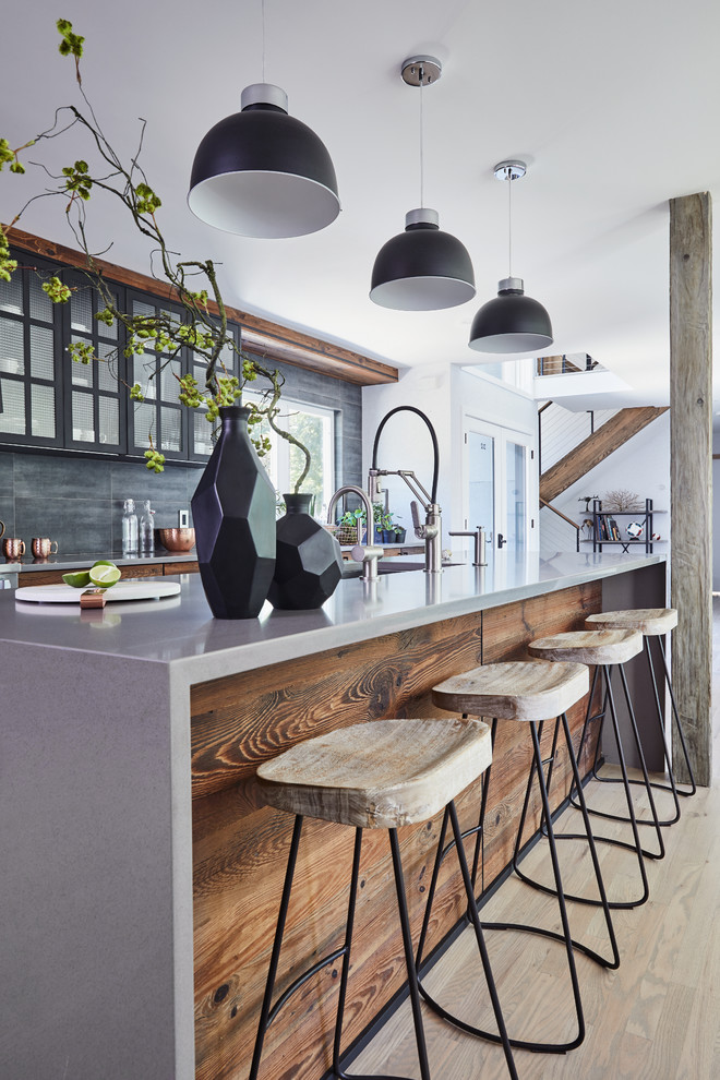 Photo of a large industrial galley kitchen/diner in New York with a submerged sink, flat-panel cabinets, dark wood cabinets, grey splashback, black appliances, light hardwood flooring, an island, beige floors and grey worktops.