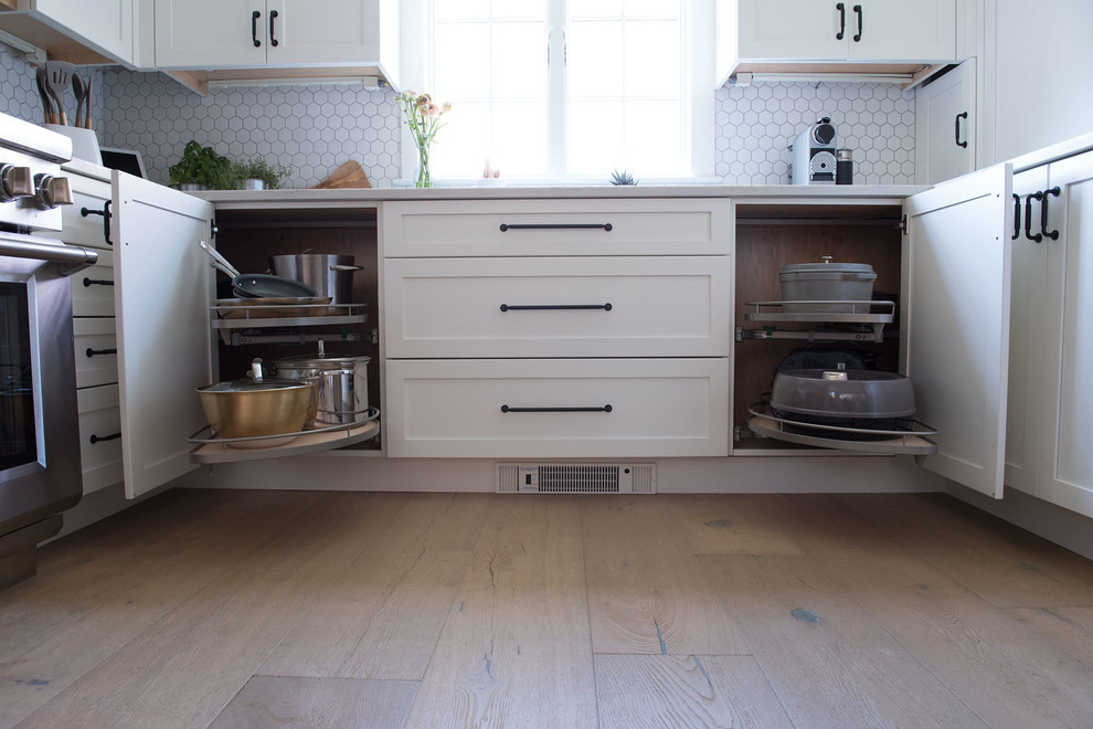 Example of a large cottage u-shaped light wood floor and brown floor eat-in kitchen design in Boston with shaker cabinets, white cabinets, quartz countertops, white backsplash, mosaic tile backsplash, stainless steel appliances, a peninsula and white countertops