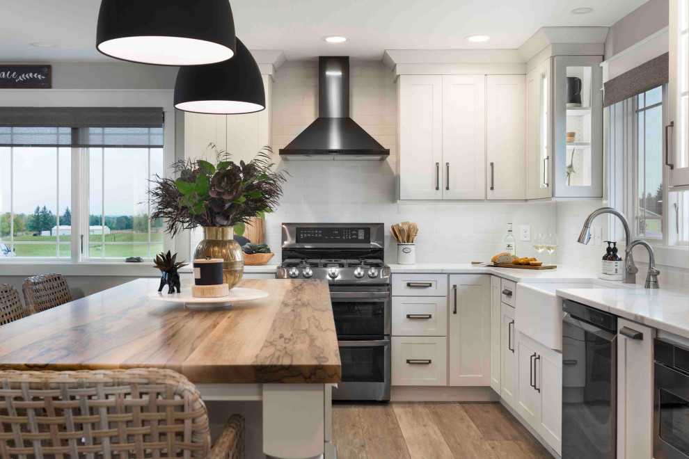 Design ideas for a medium sized traditional l-shaped kitchen in Other with a belfast sink, shaker cabinets, white cabinets, white splashback, metro tiled splashback, black appliances, medium hardwood flooring, an island, beige floors and white worktops.