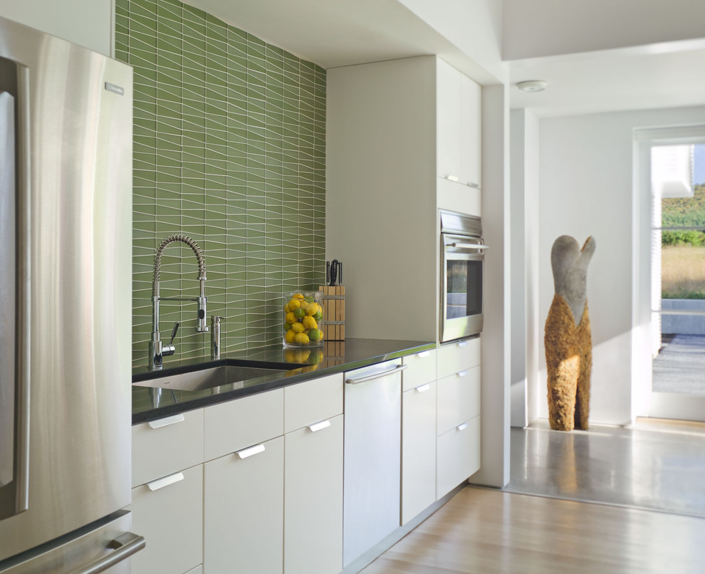 Open concept kitchen - mid-sized country single-wall light wood floor open concept kitchen idea in Burlington with stainless steel appliances, a single-bowl sink, flat-panel cabinets, white cabinets, green backsplash, granite countertops, mosaic tile backsplash and an island