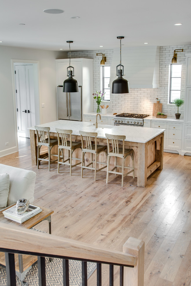 Inspiration for a large country single-wall light wood floor open concept kitchen remodel in Chicago with a farmhouse sink, recessed-panel cabinets, white cabinets, marble countertops, white backsplash, subway tile backsplash, stainless steel appliances and an island