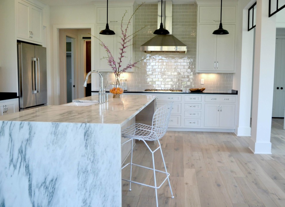 Inspiration for a large country l-shaped light wood floor open concept kitchen remodel in Indianapolis with a farmhouse sink, shaker cabinets, white cabinets, marble countertops, gray backsplash, subway tile backsplash, stainless steel appliances and an island