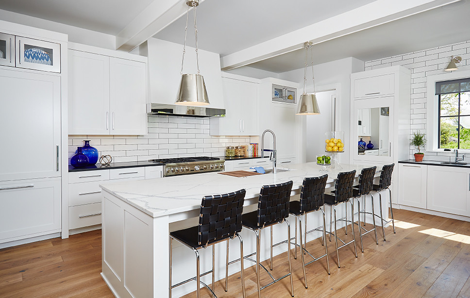 Foto på ett stort lantligt kök, med en integrerad diskho, luckor med infälld panel, vita skåp, granitbänkskiva, vitt stänkskydd, stänkskydd i tunnelbanekakel, integrerade vitvaror, mellanmörkt trägolv och en köksö