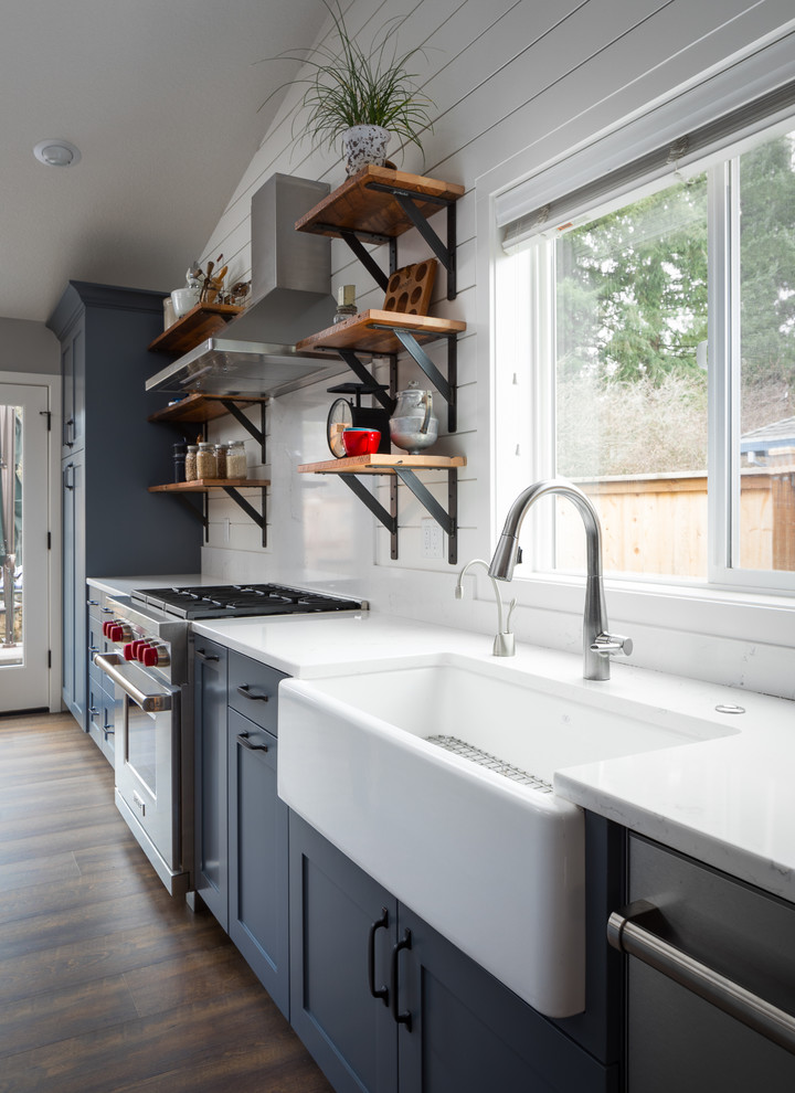 Bild på ett stort lantligt kök med öppen planlösning, med en rustik diskho, skåp i shakerstil, blå skåp, bänkskiva i kvarts, vitt stänkskydd, stänkskydd i trä, rostfria vitvaror, vinylgolv, en köksö och brunt golv
