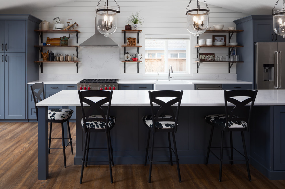 Inspiration for a large farmhouse galley vinyl floor and brown floor open concept kitchen remodel in Portland with a farmhouse sink, shaker cabinets, blue cabinets, quartz countertops, white backsplash, wood backsplash, stainless steel appliances and an island