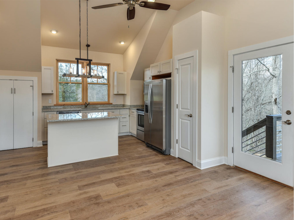 Example of a mid-sized country l-shaped medium tone wood floor and brown floor open concept kitchen design in Other with a farmhouse sink, recessed-panel cabinets, white cabinets, granite countertops, white backsplash, subway tile backsplash, stainless steel appliances and an island