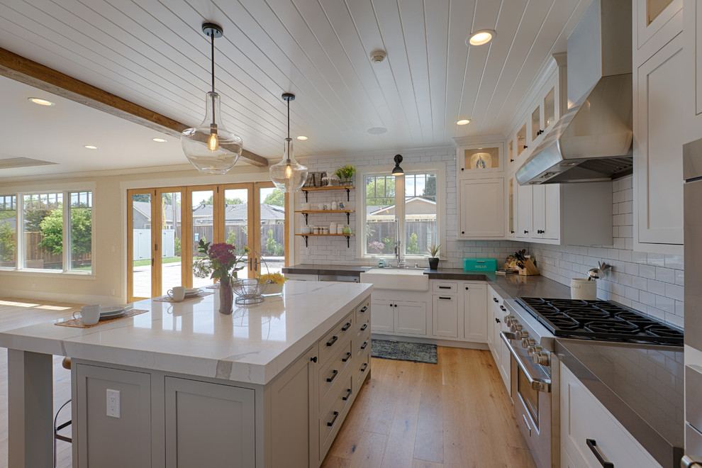 Example of a mid-sized farmhouse u-shaped beige floor open concept kitchen design in San Francisco with a farmhouse sink, white backsplash, porcelain backsplash, stainless steel appliances and an island