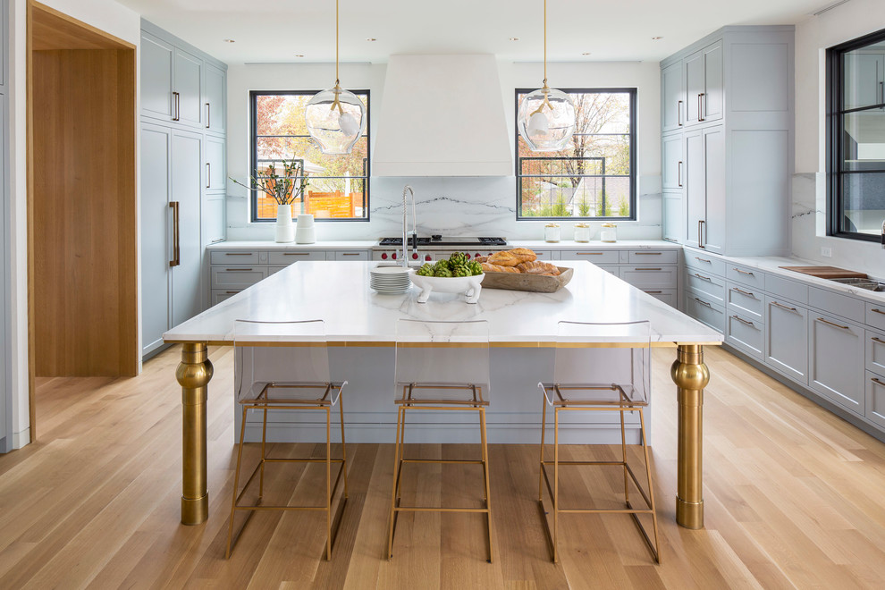 Immagine di un cucina con isola centrale chic con lavello sottopiano, ante in stile shaker, paraspruzzi bianco, elettrodomestici in acciaio inossidabile, parquet chiaro e pavimento beige
