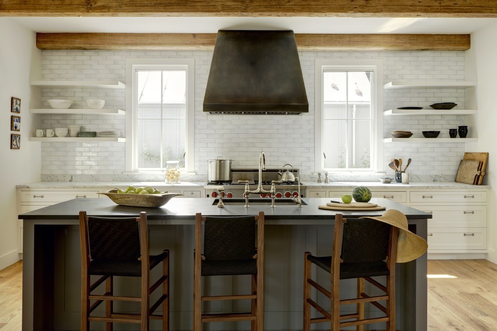 Inspiration for a farmhouse galley kitchen in DC Metro with a submerged sink, shaker cabinets, white cabinets, white splashback, metro tiled splashback, stainless steel appliances, medium hardwood flooring, an island, brown floors and white worktops.