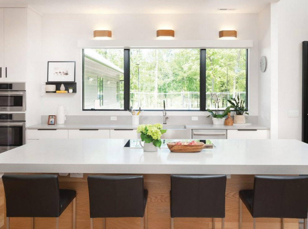 Modern inredning av ett stort grå grått kök, med en rustik diskho, släta luckor, vita skåp, bänkskiva i kvarts, rostfria vitvaror, ljust trägolv, en köksö och beiget golv