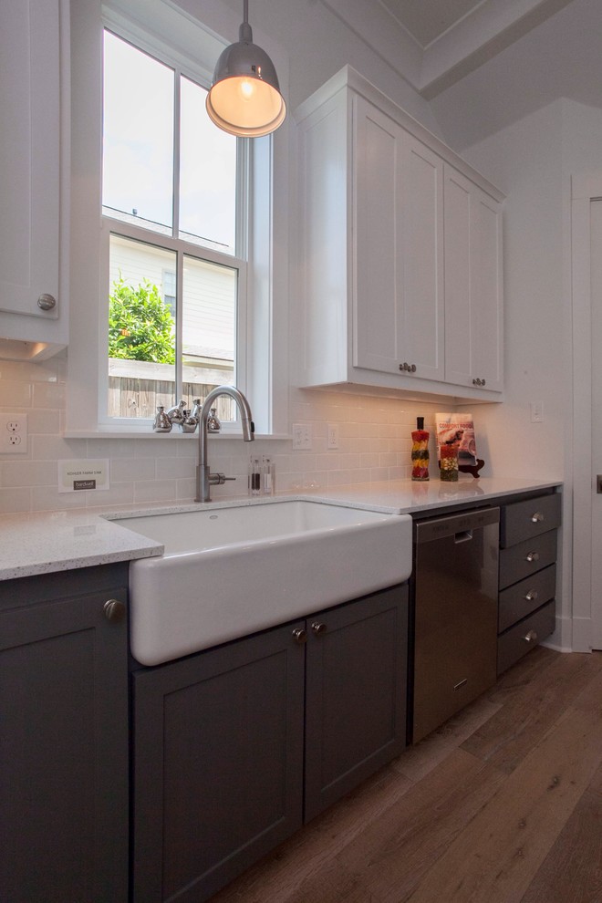Photo of a medium sized farmhouse l-shaped kitchen/diner in New Orleans with a belfast sink, raised-panel cabinets, white cabinets, granite worktops, white splashback, ceramic splashback, stainless steel appliances, light hardwood flooring and an island.