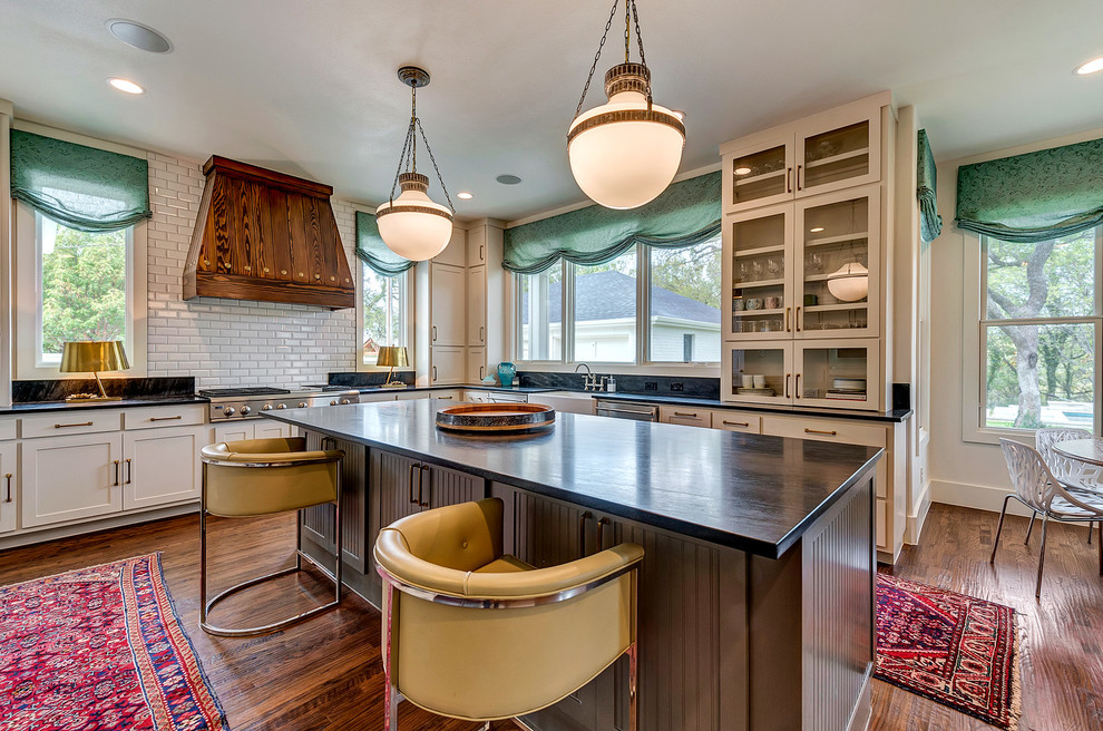 Example of a farmhouse l-shaped dark wood floor kitchen design in Dallas with a farmhouse sink, shaker cabinets, beige cabinets, white backsplash, subway tile backsplash and an island