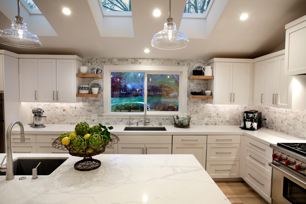 Bild på ett mellanstort lantligt vit vitt kök, med skåp i shakerstil, vita skåp, bänkskiva i kvarts, grått stänkskydd, stänkskydd i stenkakel, rostfria vitvaror, ljust trägolv, en köksö och beiget golv