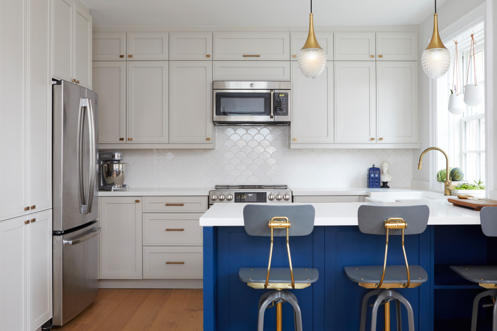 This is an example of a medium sized classic u-shaped enclosed kitchen in Toronto with a belfast sink, shaker cabinets, beige cabinets, engineered stone countertops, white splashback, mosaic tiled splashback, stainless steel appliances, light hardwood flooring, a breakfast bar, yellow floors and white worktops.