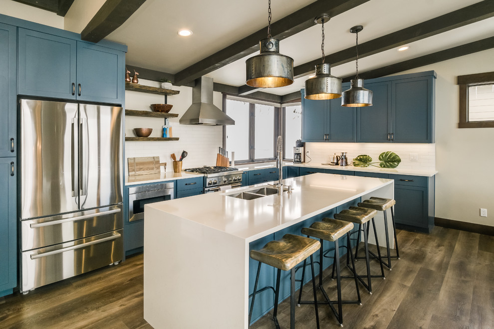 Photo of a country l-shaped kitchen in Seattle with a submerged sink, shaker cabinets, blue cabinets, white splashback, stainless steel appliances, dark hardwood flooring, an island, brown floors and white worktops.