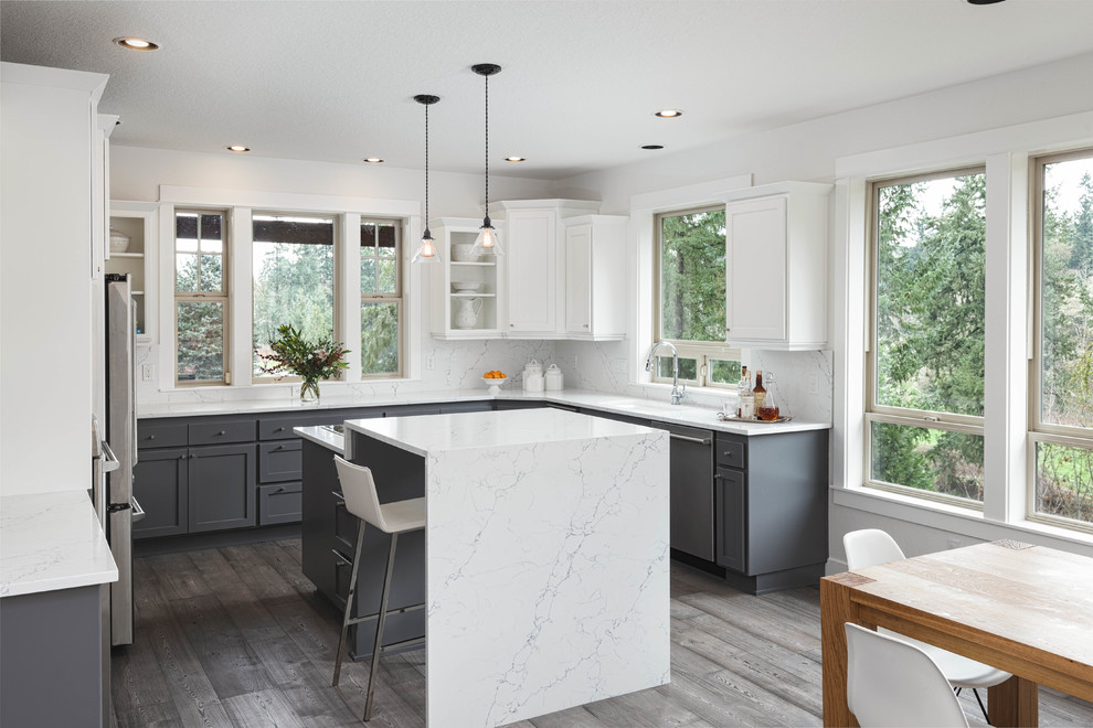 Klassisk inredning av ett kök, med en enkel diskho, skåp i shakerstil, vita skåp, marmorbänkskiva, vitt stänkskydd, stänkskydd i marmor, mörkt trägolv, en köksö och brunt golv