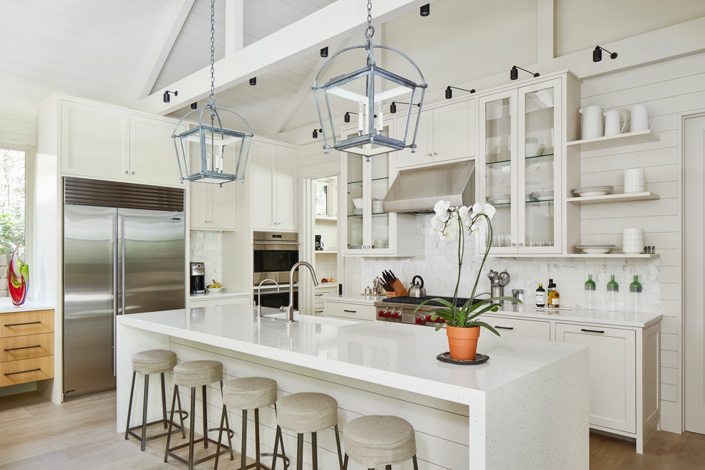 Example of a farmhouse light wood floor kitchen design in Austin with a farmhouse sink, glass-front cabinets, white cabinets, white backsplash, stainless steel appliances, an island and white countertops