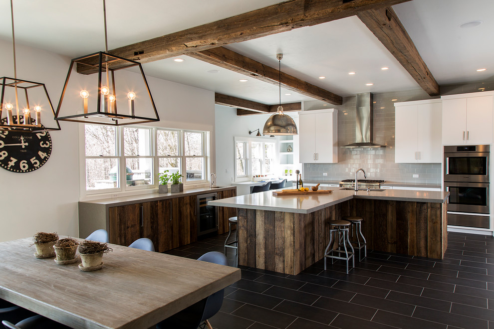 Photo of a farmhouse l-shaped kitchen/diner in Other with flat-panel cabinets, medium wood cabinets, grey splashback, metro tiled splashback, stainless steel appliances, an island and black floors.