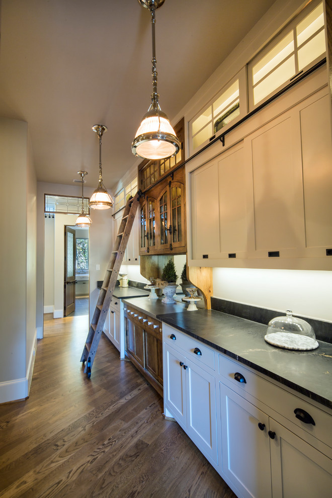 Bild på ett mellanstort lantligt linjärt kök med öppen planlösning, med en undermonterad diskho, luckor med upphöjd panel, vita skåp, granitbänkskiva, vitt stänkskydd, stänkskydd i keramik, integrerade vitvaror, mellanmörkt trägolv och en köksö