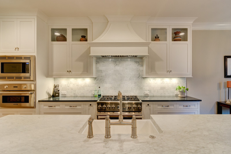 Inredning av ett lantligt mellanstort kök, med en rustik diskho, luckor med infälld panel, vita skåp, marmorbänkskiva, grått stänkskydd, rostfria vitvaror, mellanmörkt trägolv och en köksö