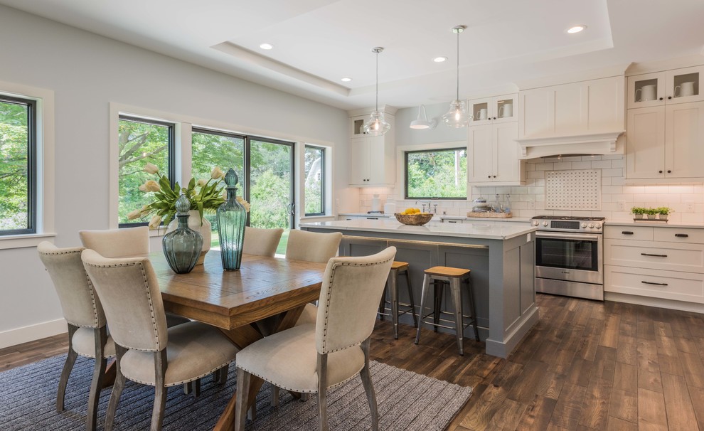 Mid-sized country u-shaped medium tone wood floor and brown floor eat-in kitchen photo in Minneapolis with white cabinets, an island, a farmhouse sink, shaker cabinets, white backsplash, stainless steel appliances, white countertops, marble countertops and subway tile backsplash